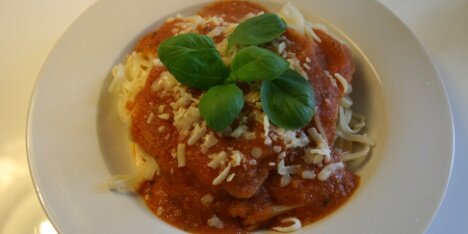 Her er tomatsaucen serveret med pasta, revet ost og frisk basilikum.