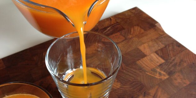 En kande fuld af appelsiner og gulerødder.