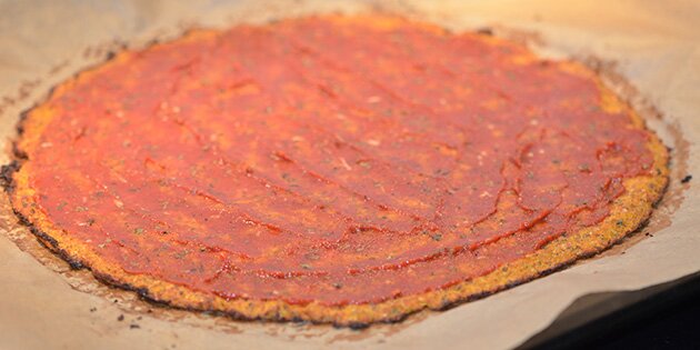 Tomat smøres på pizzabunden.