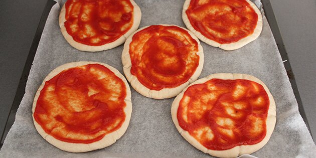 Her er tomatsaucen smurt ud på pizzaerne.