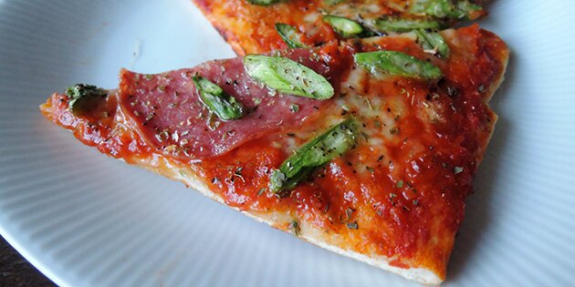 Et stykke af pizzaen med salami og asparges