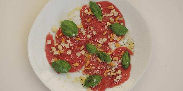 Carpaccioen serveres som forret med olivenolie, salt, peber, parmesan og pinjekerner
