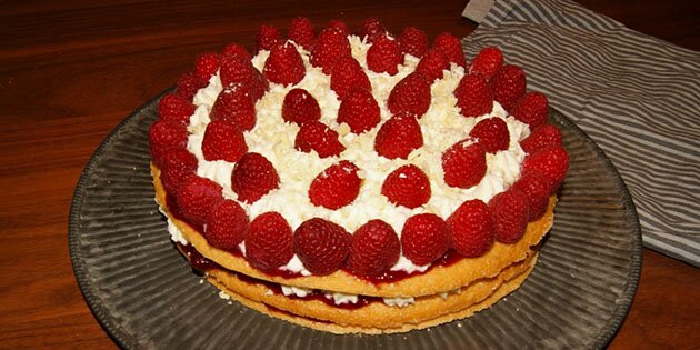 Den nemme hindbærlagkage pyntes med hvid chokolade og friske hindbær på toppen.