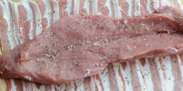 Baconen lægges ud på et skærebræt, og svinemørbraden skæres op på langs.