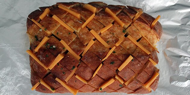 Sådan laves brødet. Hæld smørret i revnerne, og sæt skiver af ost i.