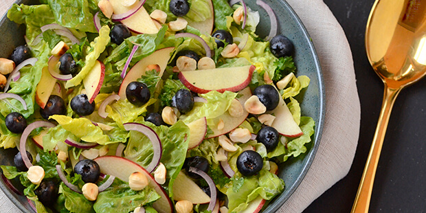 Den grønne salat toppes med friske blåbær og æblestykker og drysses med ristede hasselndøder.