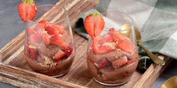 Portionsanrettet jordbær dessert i glas med kakaocreme og makroner.